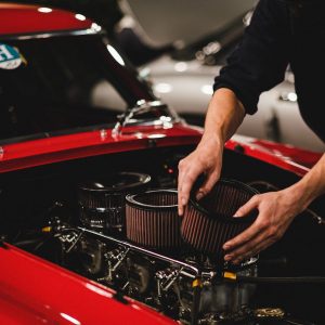 Close-up of a mechanic working on a car engine in a garage setting, focusing on air filter adjustment.